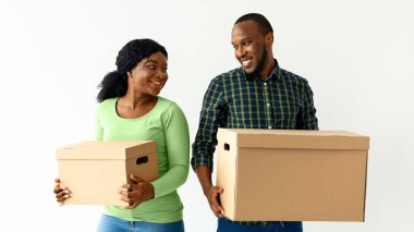 Hareketli Kavram. Karton kutular taşıyan ve birbirlerine gülümseyen mutlu siyah adam ve kadın, neşeli Afrikalı Amerikalı çift, yeni dairelerine taşınıyorlar, boş alanlarına.