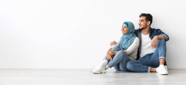 Mutlu, tesettürlü genç bir kadın, sevgi dolu kocasıyla birlikte yeni bir dairede oturuyor, ailesinin zengin geleceğini hayal ediyor, beyaz duvar arkaplanı, kopyalama alanı olan bir panorama.