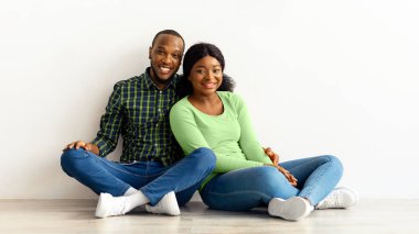 Aile Konutları. Beyaz Duvar 'ın yanında oturan mutlu siyah çift gülümseyen romantik Afrikalı Amerikalı eşler yeni evlerini, planlama yerlerini, yaratıcı kolajlarını hayal ediyorlar.