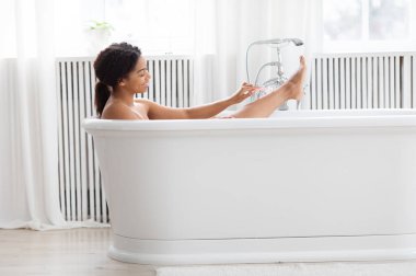 Güzel bir milenyum hanımı şık bir banyo küvetinde oturuyor ve cilt bakımını yapıyor. Kendini şımartmak ve gevşemek için bir dakika ayırırken güneş ışığı pencerelerden içeri giriyor..