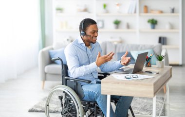 Kulaklıklı engelli bir zenci laptop üzerinden iletişim kuruyor, evden iş görüşmesi yapıyor. Milenyum Afrikalı Amerikalı tekerlekli sandalyede çağrı merkezinde çalışıyor.