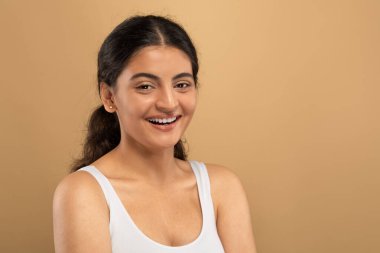 Genç bir Hintli kadın, sıcak ve tarafsız bir zemin ile çevrili cilt rutinine dalmışken gülümsüyor. Şu anda Z jenerasyonu arasında kişisel bakım ve güzellik uygulamaları sergileniyor, boşluğu kopyala