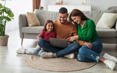 Birlikte dinleniyoruz. Orta Doğulu mutlu ebeveynlerin portresi ve şirin kızları bilgisayar kullanıyorlar, birlikte vakit geçiriyorlar, film izliyorlar ya da internette sörf yapıyorlar, oturma odasındaki halının üzerinde oturuyorlar.
