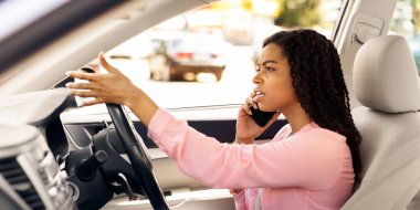 Araba kullanırken cep telefonuyla konuşan kızgın Afrikalı Amerikalı kadın portresi, cep telefonunu kullanan sinirli kadın sürücü, şehirde tartışan ve ata binen mutsuz kadın profili.