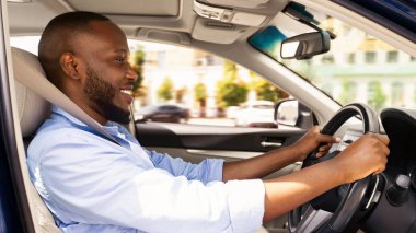 Afro-Amerikalı neşeli bir adamın araba sürüşünün, işe gidişinin ya da yaz tatilinde seyahatinin yan görünüm portresi. Gıcır gıcır arabasını süren mutlu adam galeride test sürüşü yapıyor.