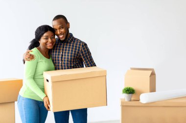 Çift Taşınma Konsepti. Mutlu siyah eşler karton kutu tutuyor ve kameraya gülümsüyor, neşeli Afro-Amerikan karısı ve kocası New House 'da duruyor, taşınmayı kutluyorlar, kopyalama alanı.