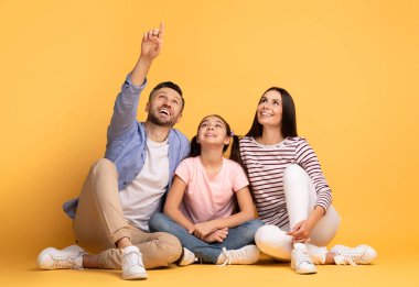 Mutlu bir aile yerde bağdaş kurup otururken gülümser. Anne ve baba yukarıdaki bir şeyi işaret eder. Heyecanlı ve neşeli görünen kızlarıyla yakınlaşırlar..