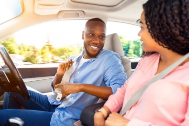 Önce güvenlik. Gülümseyen Afrikalı Amerikalı Adam ve Bayan Fastening emniyet kemerlerini şehirde sürmeden önce, yeni lüks arabanın içinde otururken, güvenli sürüş kurallarını takip ederken, yolculuğa çıkmaya hazırlanırken, birbirlerine bakarken,