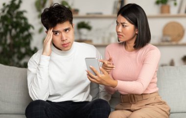Kıskanç Koreli Eş, Aldatan Kocasına Akıllı Telefonuyla Evde Koltukta Otururken Açıklama İsteğini Gösteriyor. Evlilik sorunları, kıskançlık ve sadakatsizlik İlişki Kavramında