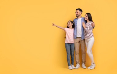 A mother, father, and their teenage daughter stand closely together, sharing smiles. The daughter points at copy space, while the parents look on with affection in a bright, cheerful setting. clipart