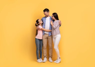 Bir baba, anne ve genç kızdan oluşan sevgi dolu üç kişilik bir aile sıcak kucaklaşmalar ve gülücükler paylaşır. Birbirlerine yakın dururlar, neşeli bir ortamda sevgi yayarlar..