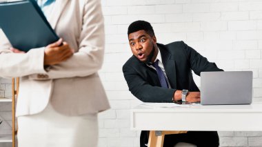 Cinsel taciz kavramı. Şok olmuş siyah bir adam iş yerinde bayan meslektaşına bakıyor.