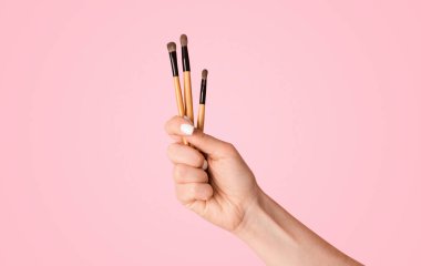 Güzellik uzmanlarının ellerinin pembe arka planda ruj ya da göz fırçası gösterdikleri yakın plan görüntüsü