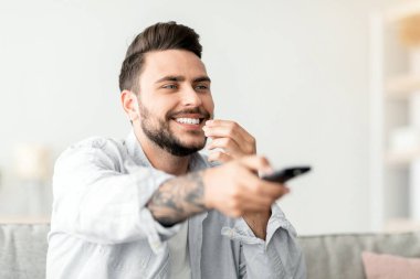 Mutlu, gevşemiş adam televizyon izliyor, patlamış mısır yiyor uzaktan kumandayla kanal değiştiriyor oturma odasında kanepede dinleniyor, fotokopi çekiyor. Genç adam hafta sonunun tadını çıkarıyor.