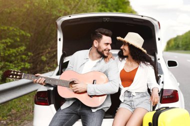 Genç beyaz adam ve kız arkadaşı bagajda bavulları ve gitarlarıyla birlikte arabayla seyahat ediyor, müzikten zevk alıyorlar. Milenyum çifti yaz tatilinde araba gezisi yapıyor, fotokopi odası.