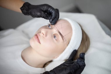 Bir kadın kuaförde uzun süreli makyaj tedavisi görüyor. Güzellik uzmanı olarak rahatlamış görünüyor. Alnı üzerinde dikkatlice çalışırken, uygulamayı kesinleştiriyor..