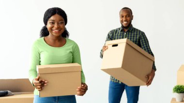 Yeni dairelerine taşınırken karton kutular taşıyan neşeli siyah eşlerin portresi, mutlu Afrikalı Amerikalı çiftler taşınma ve emlak alımını kutluyorlar.