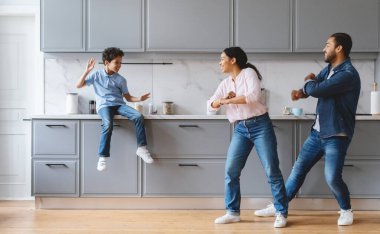 Sıcak bir mutfakta, bir anne ve baba keyifle dans ederken oğulları izliyor ve gülüyor. Aile, evlerinde sevgi ve mutluluk dolu bir anı paylaşıyor..