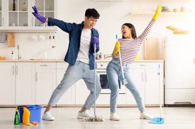 Komik Asyalı çift mutfağı temizlerken şarkı söylüyor, süpürge ve paspası mikrofon olarak kullanıyor, neşeli genç adam ve kadın rock yıldızlarını taklit ederken,