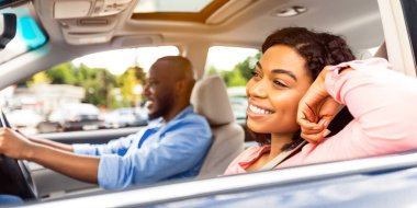 Tatil zamanı. Rahat Afro-Amerikan kadın portresi ön koltukta oturuyor ve açık pencereden dışarı bakıyor, adam modern lüks araba kullanıyor, araba yolculuğunun tadını çıkarıyor.