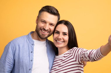 A happy European couple smiles brightly while embracing in front of a vibrant yellow background, showcasing their love and affection for one another during a playful moment. clipart