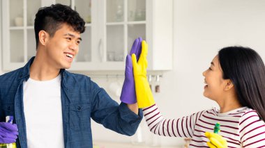Duygusal Asyalı çift ev bekçileri birbirlerine beşlik çakıyor ve gülümsüyor, yeni apartman dairesinde tam bir temizlik yapıyor renkli lastik eldivenler giyiyor, ellerinde temizlik spreyi şişeleri tutuyor, kapatıyorlar.