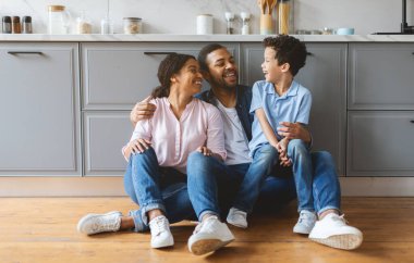 Neşeli bir aile, mutfaklarında bir anlık kahkaha paylaşır. Baba, anne ve oğul evlerinde sevgi ve sıcaklıkla çevrili bir şekilde yerde oturuyorlar..