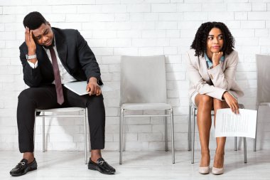 Afro-Amerikalı kadın ve erkek, ofis binasında iş görüşmesi beklemekten yorgun düşüyor. Siyahi adaylar çok uluslu şirkette açık pozisyon için başvuruyorlar.