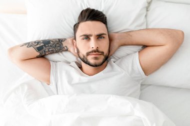 Depresyondaki genç adam uyuyamıyor, yatakta uzanıyor, yukarı bakıyor ve düşünüyor, yukarıdan bakıyor. Uykusuzluk, akıl sağlığı sorunu, erkek depresyonu kavramı