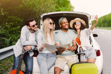 Yol boyunca haritayı kontrol eden, bagajda oturan ve yolculuklarında selfie çeken bir grup arkadaş. Çok ırklı gençler uzun bir yolculuktan sonra dinleniyorlar ve eğleniyorlar. Otostop konsepti