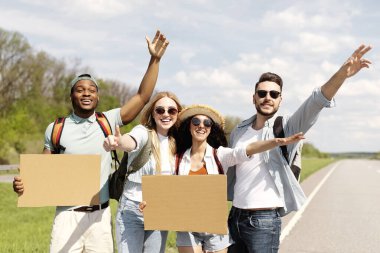 Neşeli ırklar arası arkadaşlar yol kenarında pankartlarla duruyorlar, otostop çekiyorlar, yaz tatilinde arabayı durduruyorlar, maket yapıyorlar. Turizm, birlikte seyahat, özgürlük ve arkadaşlık kavramı