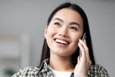 Mutlu Asyalı genç kadın kanepede oturuyor ve telefon görüşmesi yapıyor, fotokopi odasına bakıyor. Oturma odasındaki kanepede dinlenirken telefonda konuşan neşeli Koreli kadın, yakın plan portre.