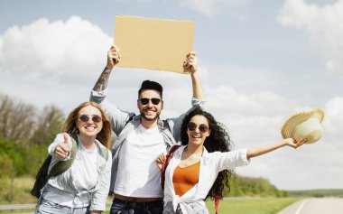 Neşeli çoklu etnik arkadaşlar otobanda boş tabelayla geziyorlar, gitar çalıyorlar, eğleniyorlar, birlikte otostop yolculuğuna çıkıyorlar, açık havada. Bir grup otostopçu yolculukta eğleniyor.