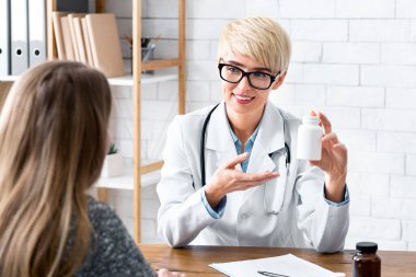 Reklamcılık ve farmakoloji konsepti. Kadın doktor elinde ilaç kavanozunu tutuyor ve hastasına