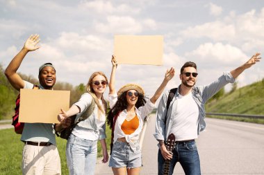 Gitarlı ve boş tabelalı çok ırklı arkadaşlar yolda otostop çekiyorlar, arabadan el sallıyorlar, otostop ile seyahat ediyorlar, maket yapıyorlar. Çok çeşitli genç insanlar yaz yolculuğuna çıkıyorlar.