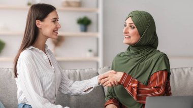 Modern Ofiste dizüstü bilgisayarın başında oturan genç bir kadınla tokalaşan olgun Müslüman iş kadını. Profesyonel Temsilci veya Danışman Danışmanla İş Toplantısı
