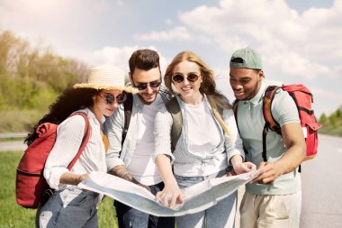 Yol boyunca harita kontrolü yapan, otostop çeken sırt çantalı bir grup arkadaş. Çok ırklı genç turistler rotalarını çiziyor, yaz tatillerinde otostop çekiyorlar.