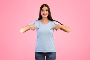 Choose Me. Portrait of positive female model pointing at herself, wearing blue t-shirt for your text or promotional content, indicating chest, advertising concept, lady isolated over yellow background clipart