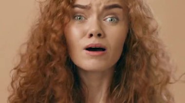 Kıvırcık saçlı genç bir kadın ellerini kaldırırken şaşkınlık ve endişeyle karışık duygular gösterir. Canlı yeşil gözleri ve hareketli ifadesi yoğunluğunu yansıtıyor..