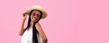 Afro demetli oyuncu zenci kadın pembe stüdyo arka planında boş alana bakıyor, panorama. Moda kıyafetli, poz veren ve gülümseyen Afrikalı Amerikalı genç bir kadının portresi.