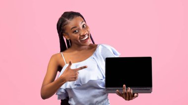 Güzel siyah kadın pembe stüdyo arka planında boş ekranlı dizüstü bilgisayarı gösteriyor. Model için yer var. Neşeli Afrikalı Amerikalı kadın taşınabilir bilgisayarı şablonla tutuyor.
