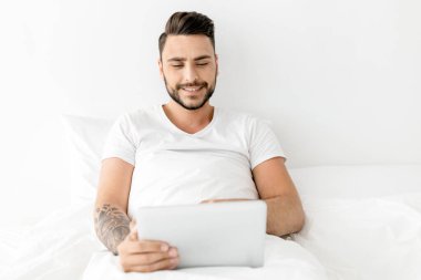 Mutlu adamın portresi battaniyenin altında yatar ve bilgisayar kullanır, dizüstü bilgisayarla klavyeye yazar, internette gezinir, çalışır ya da dinlenir.