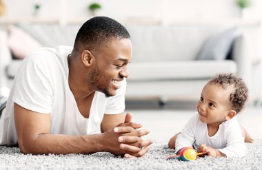 Baba Bebek Bağlantısı. Mutlu siyahi adam evde tatlı çocukla kaynaşıyor, Afrikalı Amerikalı baba ve sevimli çocuğu oturma odasında yerde dinleniyor, boş yer var.