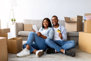 Dijital tabletli ve kredi kartlı siyah çift yeni bir daireye taşındıktan sonra mobilyalarını internetten seçiyorlar. İnternet üzerinden alışveriş yapan mutlu eşler