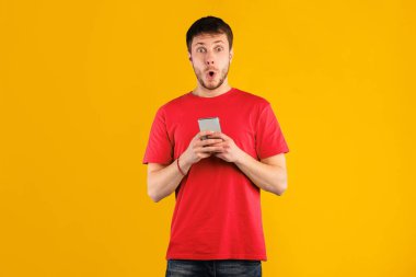 Vay canına, Harika Uygulama. Heyecanlı genç adamın portresi cep telefonu kullanıyor mavi stüdyo arka planında izole edilmiş, kopyalama alanı. Tokatlanmış adam internette konuşuyor, kameraya bakıyor.