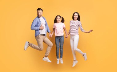 Neşeli bir aile, canlı sarı bir zemin karşısında birlikte duruyor. Ebeveynler genç kızlarıyla el ele tutuşup neşeli pozları ve gülümsemeleriyle sevgi ve neşe ifade ederler..