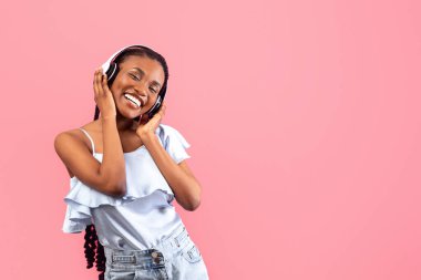 Kablosuz kulaklıklı mutlu siyah kadın pembe stüdyo arka planında popüler müzik dinliyor. Neşeli Afrikalı Amerikalı kadın favori şarkı ya da havalı şarkı listesinin keyfini çıkarıyor.