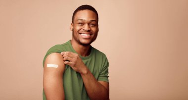 Covid-19 Aşılama. Coronavirus antiviral aşıdan sonra kollarını gösteren mutlu Afrikalı adam portresi bej arka planda çekildi. Kapsamlı Dokunulmazlık Kampanyası Kavramı. Panorama
