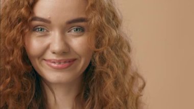 Kıvırcık kızıl saçlı ve çarpıcı yeşil gözlü genç bir kadın doğal güzelliğini ve özgüvenini sergileyerek kameraya doğrudan tarafsız bir arkaplana bakıyor..