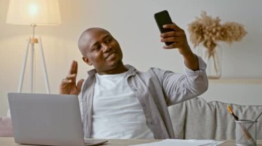 Parlak ve davetkar bir oturma odasında, 30 'lu yaşlarda Afro-Amerikalı bir adam akıllı telefonuyla bir video görüşmesi yaparken gülümsüyor..